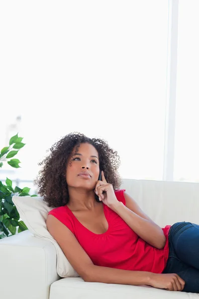 Frau, die anruft, während sie aufblickt, auf der Couch sitzend — Stockfoto