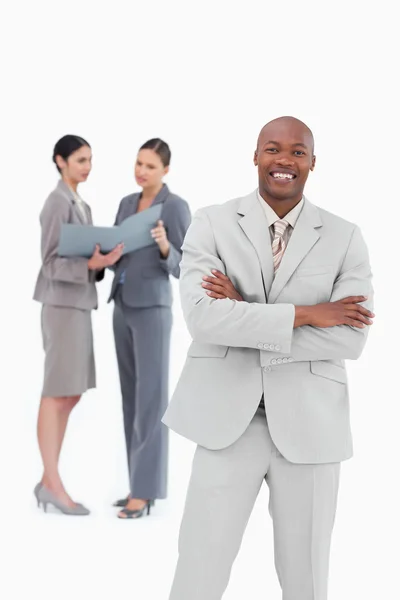 Smiling salesman with arms crossed and co-workers behind him — Stock Photo, Image