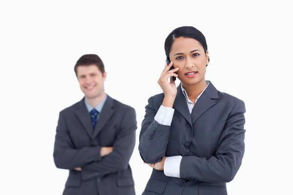 Close up of serious saleswoman on the phone with co-worker behin — Stock Photo, Image