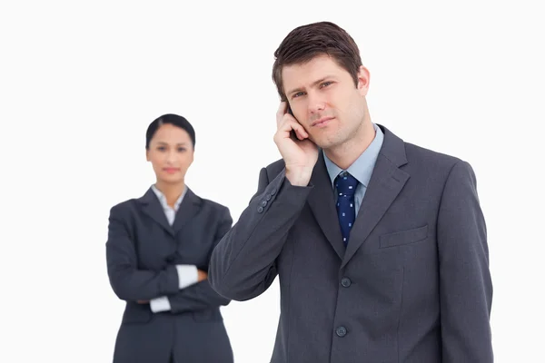 Close up de vendedor ao telefone com colega atrás dele — Fotografia de Stock