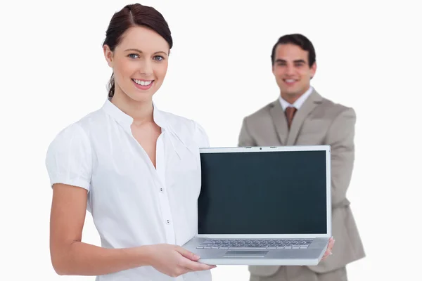 Smiling saleswoman presenting laptop screen with colleague behin — Stock Photo, Image