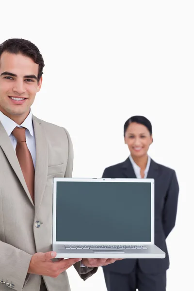 Laptop being presented by smiling salesman with colleague behind — Stock Photo, Image