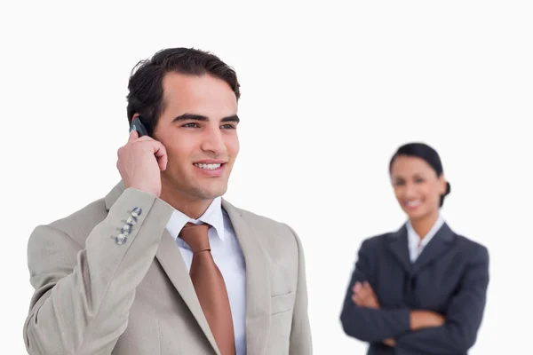 Smiling salesman on his mobile phone with colleague behind him — Stock Photo, Image