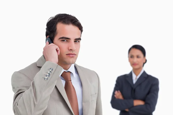 Serious salesman on his cellphone with colleague behind him — Stock Photo, Image