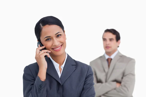 Smiling saleswoman on her mobile phone and colleague behind her — Stock Photo, Image