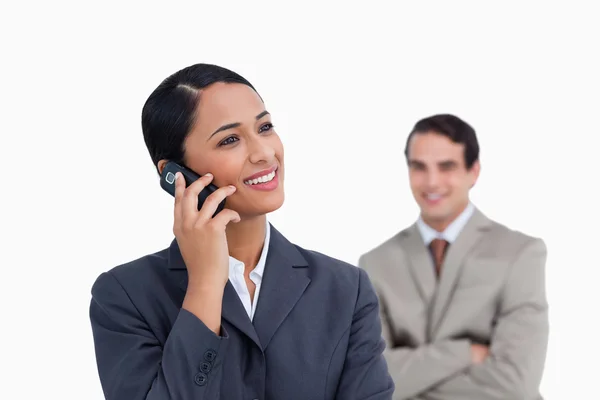 Lächelnde Verkäuferin auf ihrem Handy und ein Kollege hinter ihr — Stockfoto