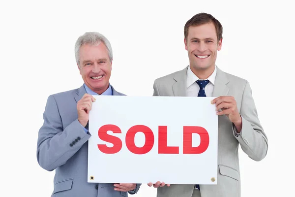 Agentes inmobiliarios sonrientes sosteniendo letrero vendido —  Fotos de Stock