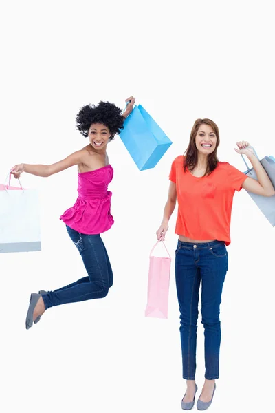A teenage girl jumping with her shopping bags while her friend i — Stock Photo, Image