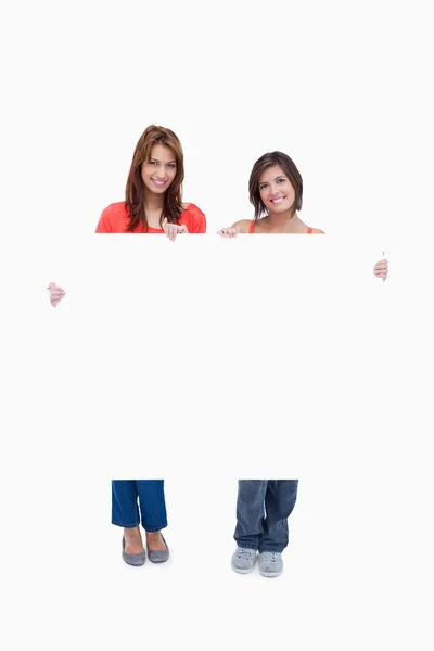Deux adolescentes souriantes tenant une affiche vierge contre un blanc — Photo