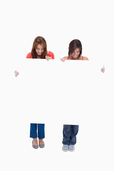 Duas meninas adolescentes sorrindo enquanto olham para seu cartaz em branco — Fotografia de Stock