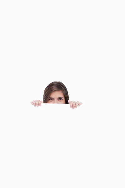 Menina adolescente feliz se escondendo atrás de um cartaz em branco — Fotografia de Stock
