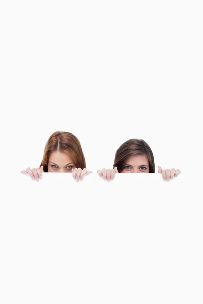 Two friends secretly hiding behind a blank poster — Stock Photo, Image