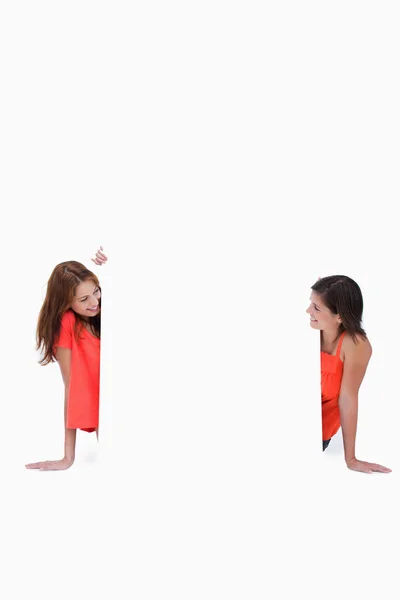 Teenage girls looking at each other in front of a blank poster — Stock Photo, Image