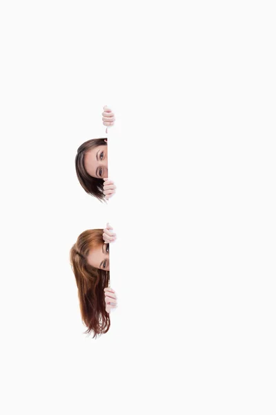 Zwei Teenager-Mädchen bekommen ihre Köpfe aus einem leeren Plakat — Stockfoto