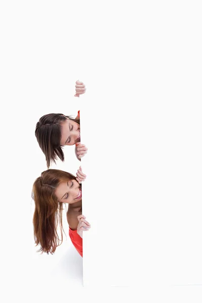 Adolescentes escondidos atrás de um cartaz em branco enquanto mostram suas cabeças — Fotografia de Stock