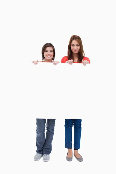 Mulheres jovens sorridentes orgulhosamente segurando um cartaz em branco — Fotografia de Stock