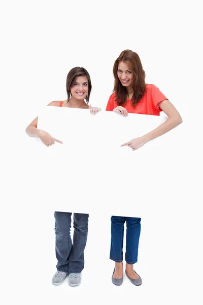 Smiling teenage girls standing upright behind a blank poster whi — Stock Photo, Image
