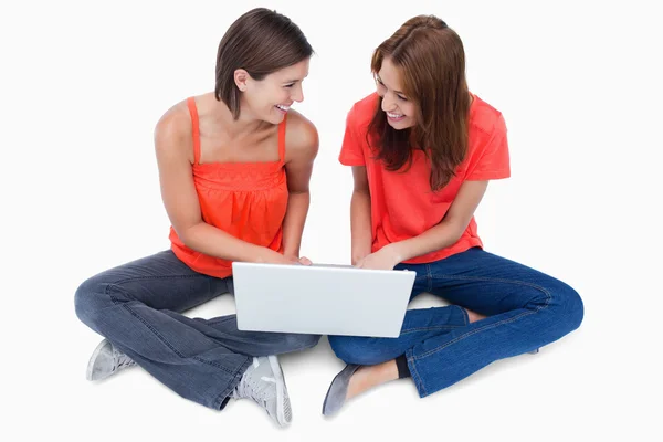 Adolescentes sonrientes sentados con las piernas cruzadas con una computadora portátil —  Fotos de Stock