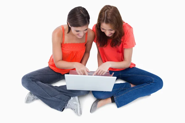Two cute teenagers sitting cross-legged while looking at a lapto — Stock Photo, Image