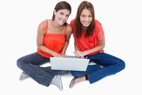 Sonriendo chicas adolescentes sentadas con una computadora portátil en las piernas mientras miran — Foto de Stock