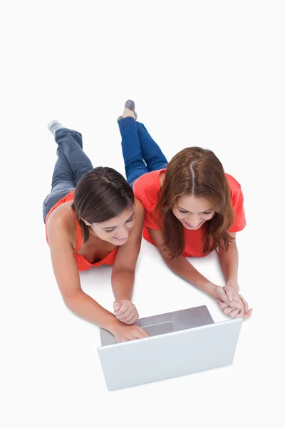 Twee glimlachend tienermeisjes liggen tijdens het kijken naar een laptop — Stockfoto