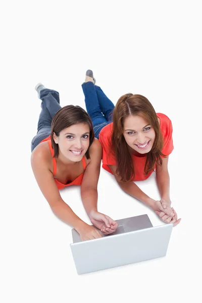 Twee aantrekkelijke tienermeisjes liggen met een laptop tijdens het kijken — Stockfoto