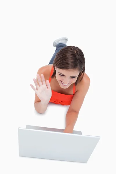 Attractive young woman saying hello to her computer while lying — Stock Photo, Image