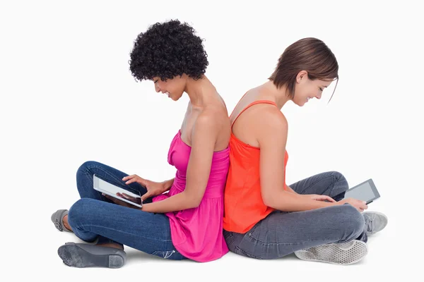 Adolescentes sentados con las piernas cruzadas espalda con espalda con un comprimido —  Fotos de Stock