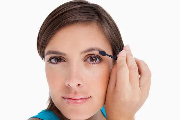 Młoda kobieta, patrząc na kamery, wprowadzenie eyeshadow na jej eyeli — Zdjęcie stockowe