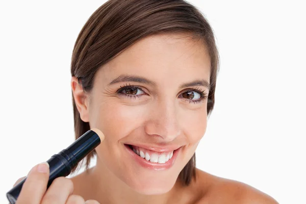 Mujer joven sonriente aplicando una base natural en su cara — Foto de Stock
