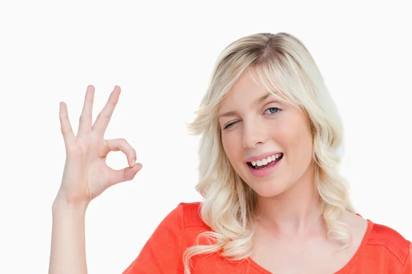 Junge blonde Frau zeigt das Okay-Zeichen und einen Wimpernschlag — Stockfoto