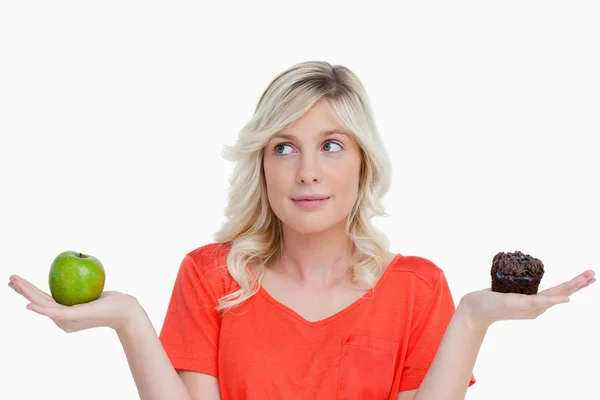 Woman hesitating between a chocolate muffin and a green apple — Stock Photo, Image