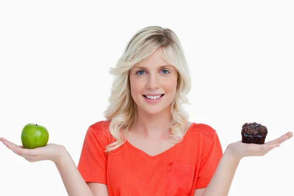 Woman beaming while holding a chocolate muffin and a green apple — Stock Photo, Image