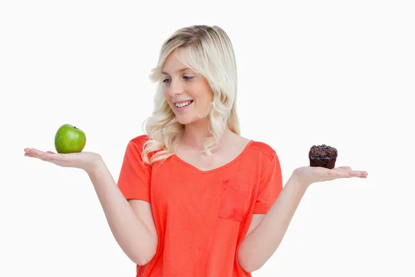 Mujer joven sosteniendo una manzana y un panecillo mientras mira el a — Foto de Stock