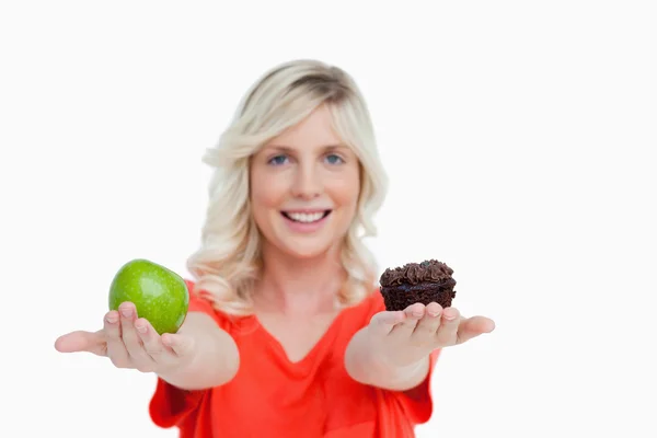 Женщина держит яблоко в правой руке и кекс в левой. — стоковое фото