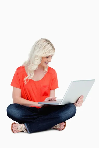 Mladá blondýnka sedět se zkříženýma nohama s laptopem na její l — Stock fotografie