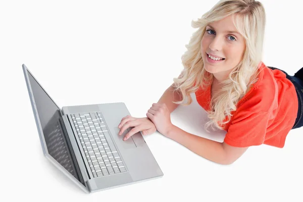 Wanita muda tersenyum menggunakan laptopnya saat berbaring — Stok Foto