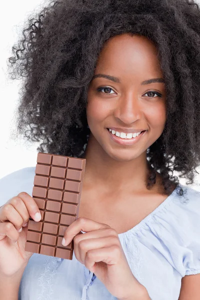 Mujer joven sonriente con el pelo rizado sosteniendo una barra de chocolate —  Fotos de Stock