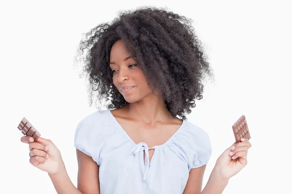 Jovem mulher olhando para um de seus dois pedaços de chocolate — Fotografia de Stock