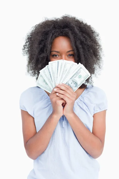 Jovem mulher encaracolada escondendo seu rosto atrás de um fã de dólares — Fotografia de Stock