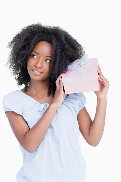 Mujer joven mirando a un lado mientras sacude un regalo — Foto de Stock