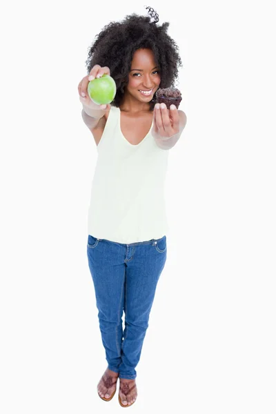 Mujer joven sonriente sosteniendo una manzana en una mano y un panecillo en — Foto de Stock