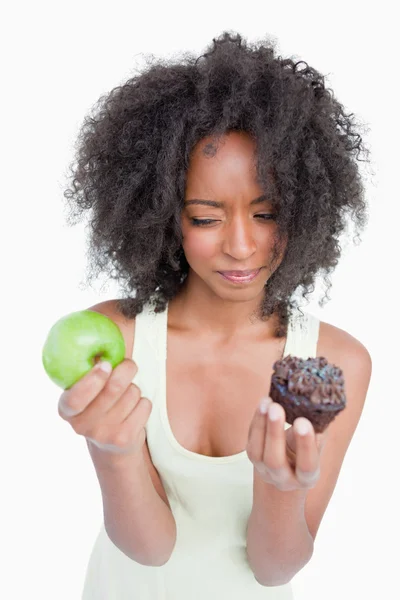 Junge Frau zögert zwischen Schokoladenmuffin und grünem Apfel — Stockfoto