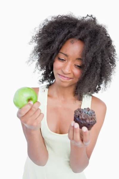 Young woman hardly hesitating between a muffin and an apple — Stock Photo, Image