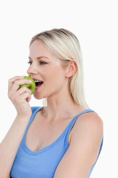 Femme blonde regardant vers le côté tout en mangeant une pomme verte — Photo