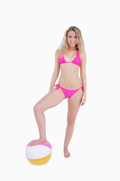 Sonriente adolescente atractiva colocando su pie en una pelota de playa — Foto de Stock