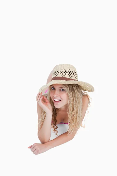 Adolescente sorridente deitada enquanto segurava a aba do chapéu — Fotografia de Stock