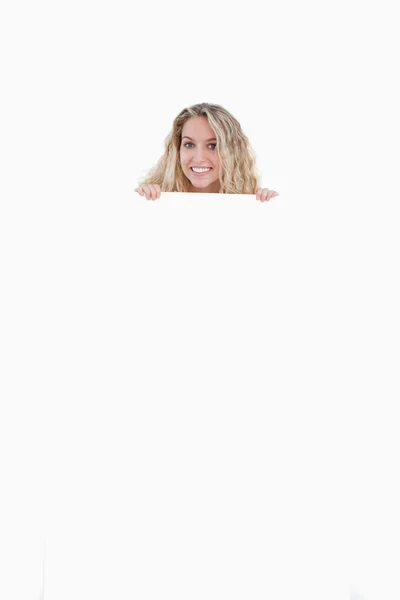 Smiling young woman hiding her body behind a blank poster — Stock Photo, Image