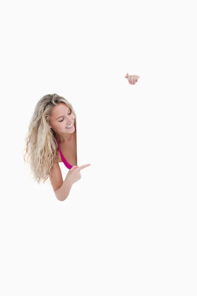 Jovem mulher sorridente apontando o dedo para um cartaz em branco — Fotografia de Stock