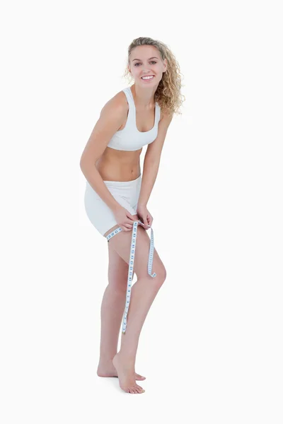 Sorridente giovane donna misurare la coscia con un nastro di misura — Foto Stock